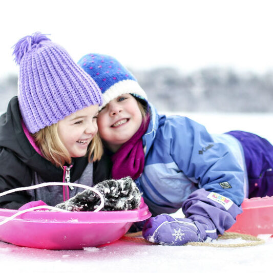 2 little girls on sleds in the snow laughing